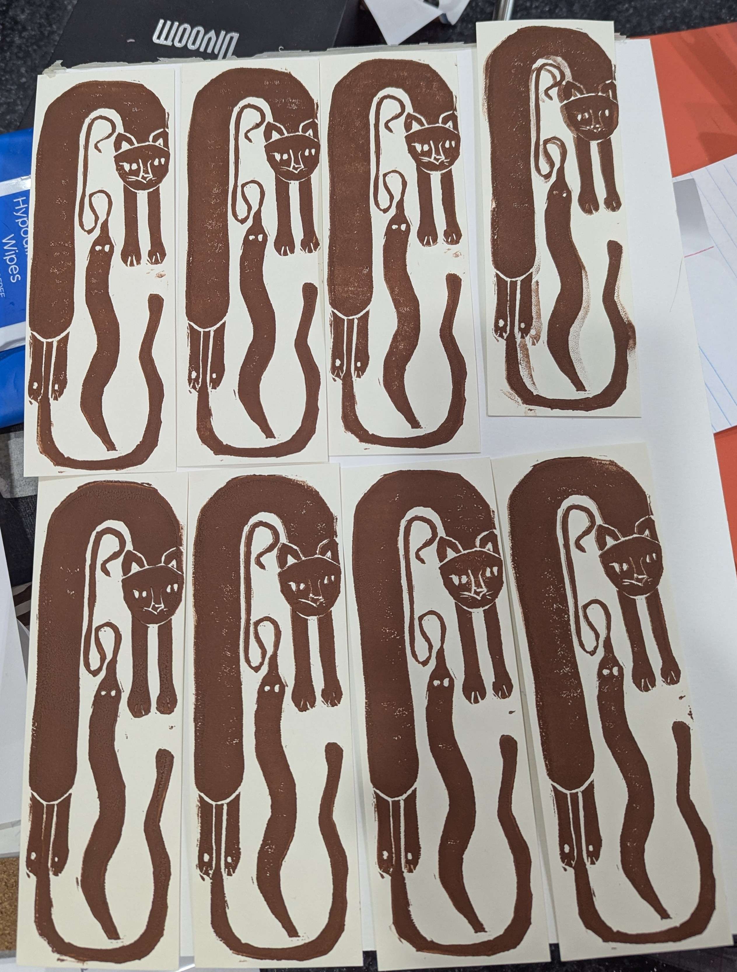 Linocut bookmarks of a cat chasing his tail and a worm-on-a-string in the middle.